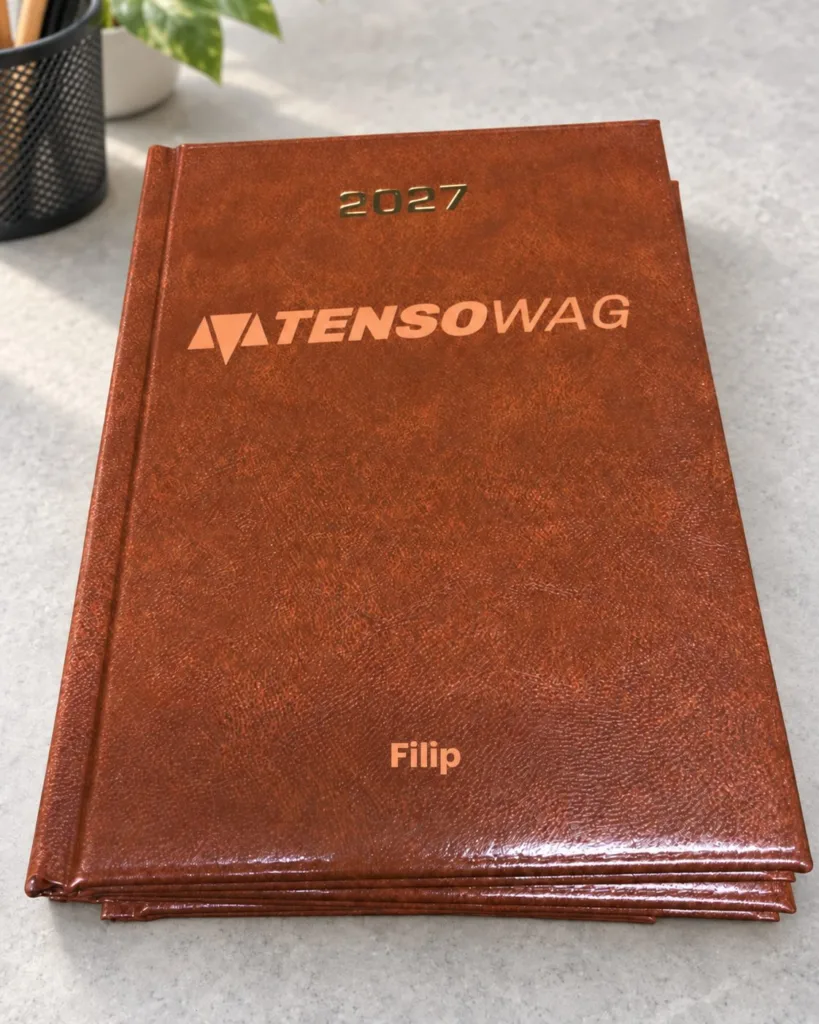 Stos brązowych kalendarzy 2027 z logo TENSOWAG i imieniem Filip, aranżacja.