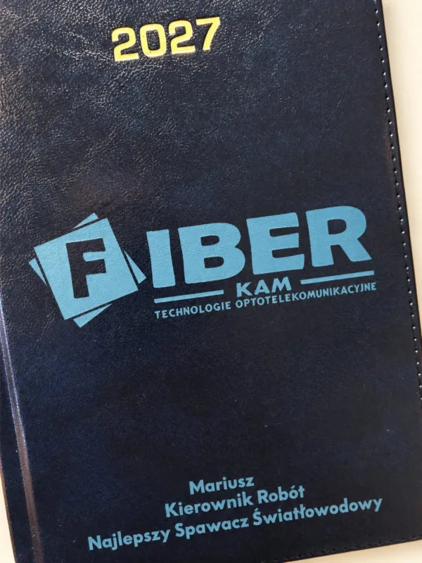 Granatowy kalendarz 2027 z logo FIBER KAM, imieniem i stanowiskiem, aranżacja.